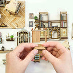 Hands assembling a small Pastoral furnishing beside miniature wall panels and cottage decorations.