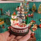 Hand holding a Snowy Christmas Lodge snowman display with tiny gifts and a signpost.